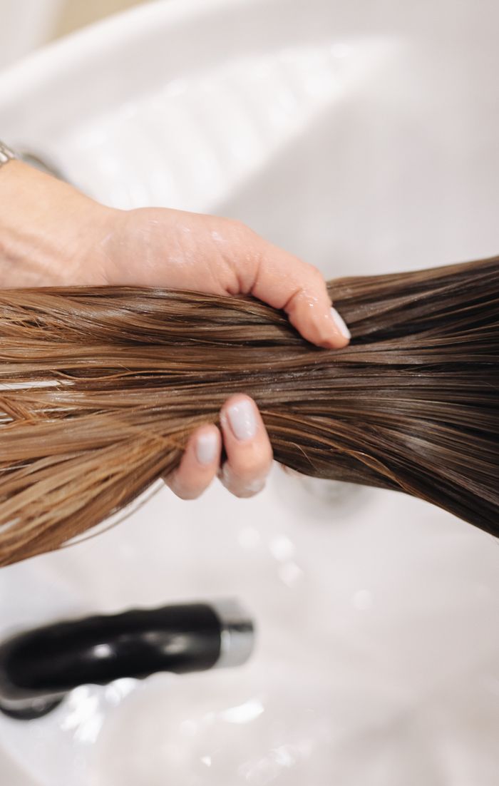 Close-up of a hand holding wet hair in a salon sink, showcasing hair treatment.